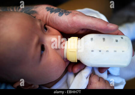 Fathers hand feeding bottled milk to baby son Stock Photo