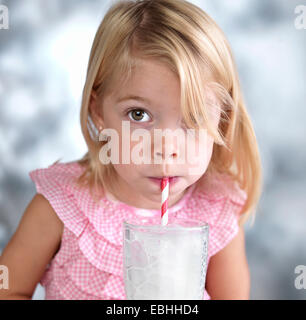 Portrait of female toddler blowing bubbles in milk through drinking straw Stock Photo
