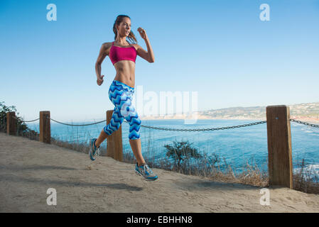 Young woman running on path by sea Stock Photo