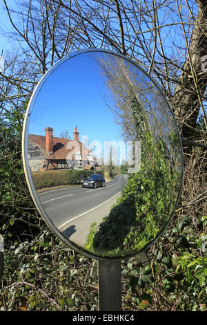 Convex glass safety mirror used to aid exiting concealed drive in country lane. Surrey England UK Stock Photo