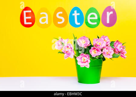 Pink flowers in green pot on table, word Easter Stock Photo
