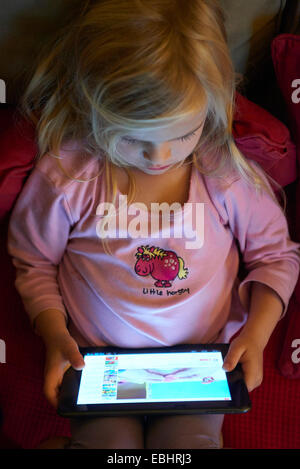 Blond child girl using (playing, watching) digital tablet on couch at night Stock Photo