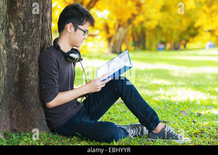 Man reading book in park, sitting under a tree. Relaxing outdoors reading. Stock Photo