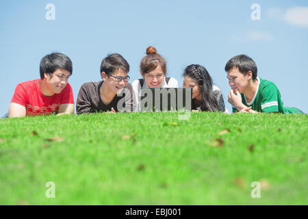Group of students outdoors lying on grass and looking computer Stock Photo