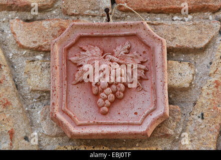 Decorative ceramic tile with grape vine fixed on a brick wall outside a wine bar / shop in Italy, Europe. Stock Photo