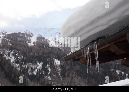 Heavy snow and icicles on rooftop. Snowy mountains in background. Winter scene. Valle d'Aoste, Italy. Stock Photo