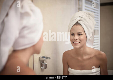 Young woman wearing towel on head looking at reflection in mirror Stock Photo