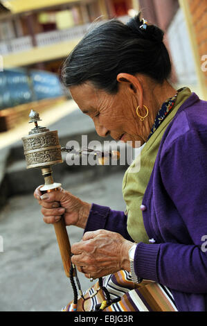 old buddhist woman in a monastry  is sunk in a prayer with a prayer wheel in the hand, Nepal, Pokhara Stock Photo