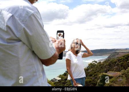 Husband photographing wife, ocean in background, Raglan, New Zealand Stock Photo