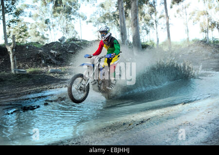 Young male motocross rider splashing through forest river Stock Photo