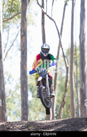 Young male motocross rider jumping mid air in forest Stock Photo