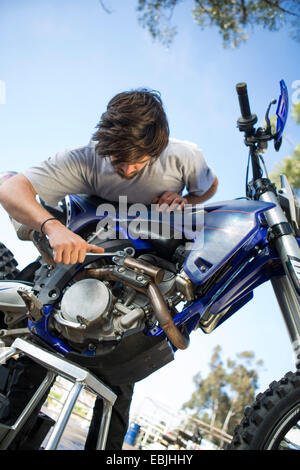 Young male motocross racer adjusting motorcycle engine in forest Stock Photo