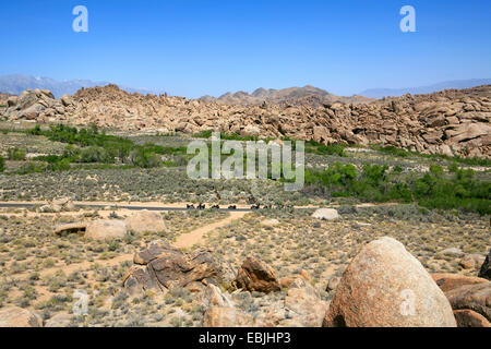 panoramic view over the plains and boulder-like rock formations of the Alabama Hills with some bikers resting at the edge of a country road, USA, California, Lone Pine Sanctuary Stock Photo