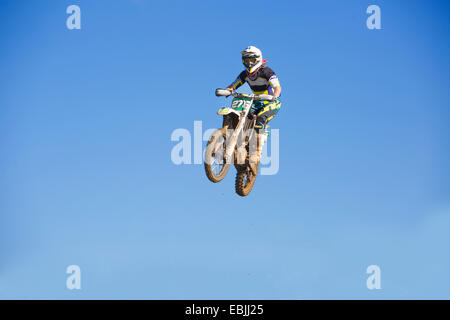 Young male motocross racer jumping mid air against blue sky Stock Photo