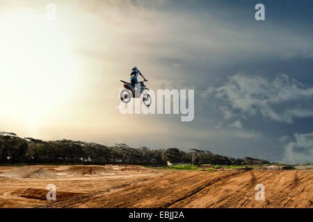 Silhouetted young male motocross racer jumping mid air over mud track Stock Photo