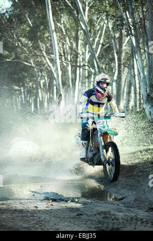 Young male motocross racer riding through puddle in forest Stock Photo