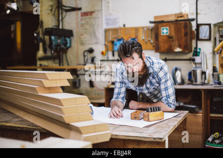 Mid adult craftsman looking down at blueprint in organ workshop Stock Photo