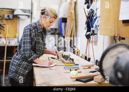 Young craftswoman making notes at workbench in pipe organ workshop Stock Photo