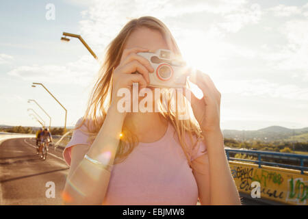 Young woman on bridge taking photographs on digital camera Stock Photo