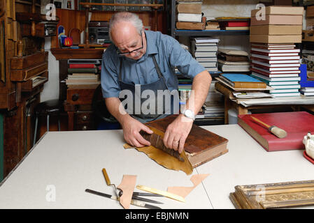 Senior man repairing antique book spine in traditional bookbinding workshop Stock Photo