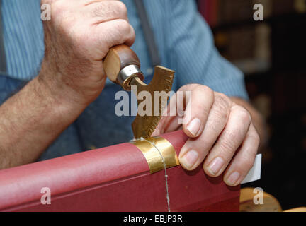 Close up of hands of senior male traditional bookbinder pressing gold leaf onto book spine Stock Photo