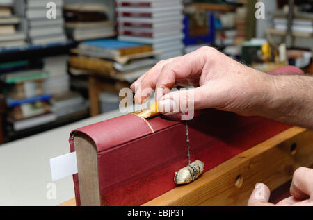 Close up of hands of senior male traditional bookbinder applying gold leaf to book spine Stock Photo