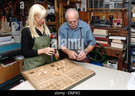 Senior man and young woman assembling book letterpress in traditional bookbinding workshop Stock Photo