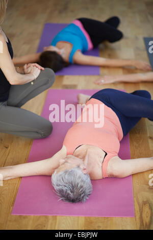 Female students lying on back and twisting hips in pilates class Stock Photo