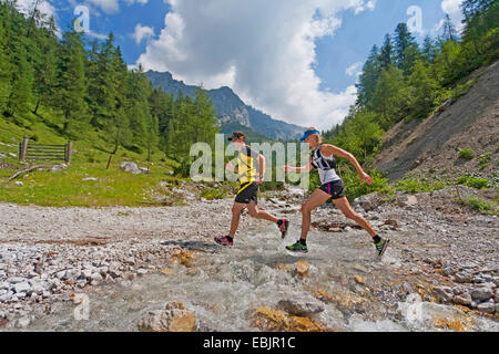 young couple crossing a brook by jumping while trail running in the Dachstein Mountains, Austria, Styria, Dachstein Stock Photo