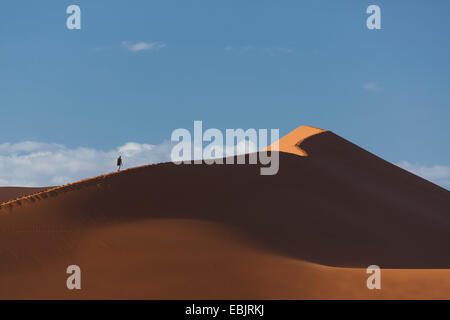 Silhouetted man climbing giant sand dune, Sossusvlei National Park, Namibia Stock Photo