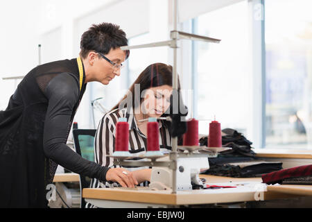 Two seamstresses looking down at sewing machine in workshop Stock Photo