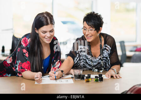 Two seamstresses painting fashion design on work table