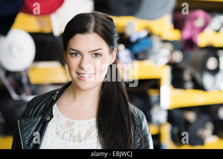Portrait of young seamstress in front of textile shelves in workshop