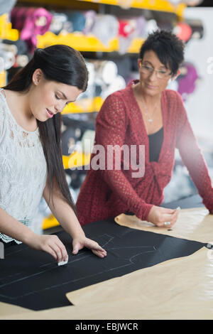 Two seamstresses chalking outline onto textile on work table Stock Photo