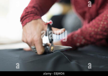 Close up of seamstress hands using scissors to cut textile at work table Stock Photo