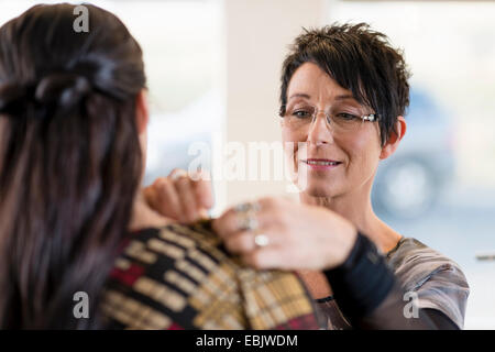 Mature seamstress adjusting shoulder of customers dress in workshop