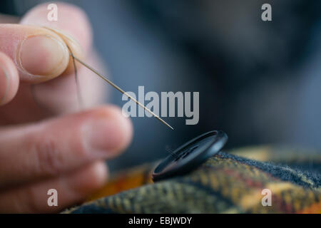 Close up seamstress fingers sewing button onto tartan in workshop Stock Photo