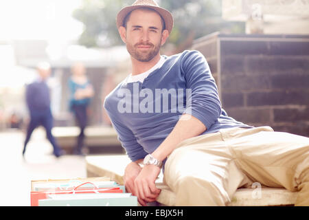 Mid adult man relaxing on seat, shopping bags beside him Stock Photo