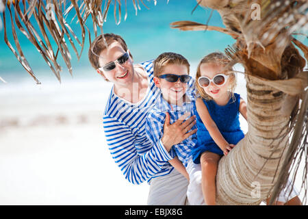 father and two kids sitting on palm trunk at tropical beach, Mexico