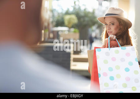 Woman holding shopping bags, looking over shoulder at man Stock Photo