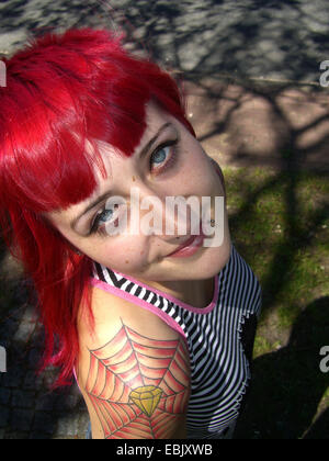 young tattooed redheaded woman looking up to the camera Stock Photo