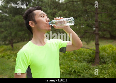 Young male runner drinking bottled water in park