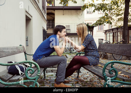 Young couple holding hands from opposite park benches Stock Photo