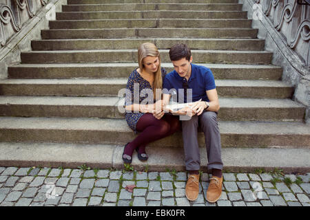 Young couple sitting on old street stairway reading newspaper Stock Photo