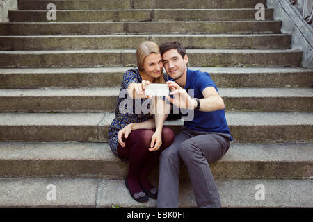 Young couple sitting on old street stairway posing for smartphone selfie Stock Photo