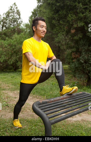 Young male runner stretching leg on park bench in park Stock Photo