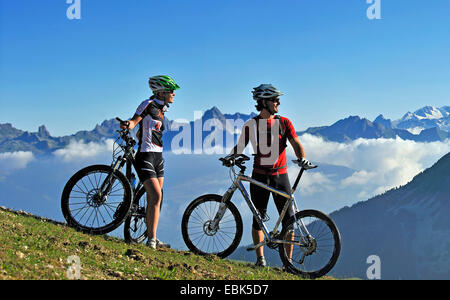 two mountain biker standing on mountain meadow and enjoying the mountain scenery, France, Savoie, La Plagne Stock Photo
