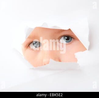 little boy looking through hole in a white paper surface Stock Photo