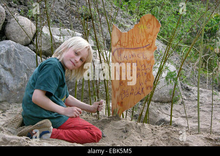 boy in the garden has discovered a wild bee nest in the sand and protects it with a sign and a little willow fence, Germany Stock Photo
