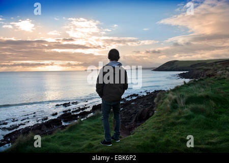 A teenage boy listens to his iPod while looking at the view at Manorbier Bay near Tenby in Pembrokeshire, Wales UK Stock Photo